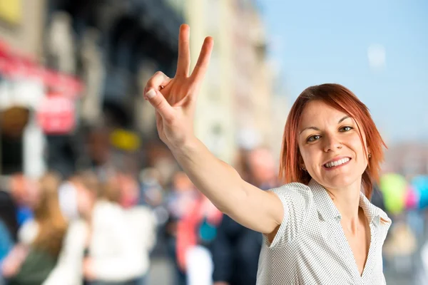 Jonge vrouw doen overwinning gebaar op witte achtergrond — Stockfoto