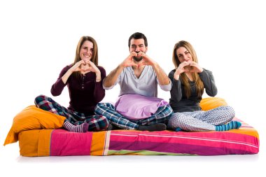 Üç arkadaş bir yatakta kendi elleriyle bir kalp yapma