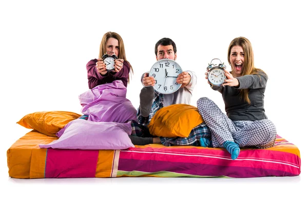 Three friends on a bed holding vintage clock — Stock Photo, Image