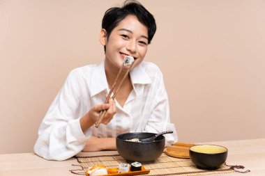 Genç Asyalı kız bir kase erişte ve suşiyle masada.