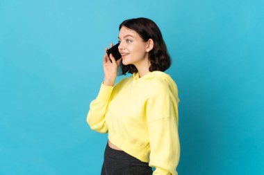 Genç Ukraynalı kız mavi arka planda izole edilmiş cep telefonuyla sohbet ediyor.