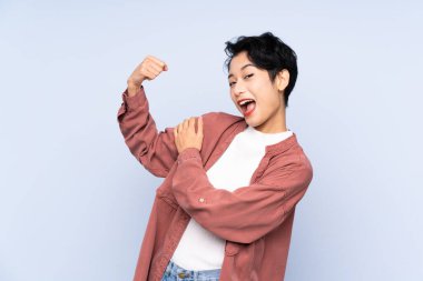 Soyutlanmış mavi arka planda genç Asyalı kız güçlü bir jest yapıyor.