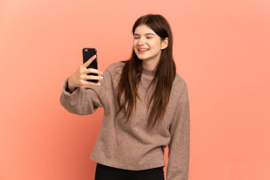 Pembe arka planda izole edilmiş genç Ukraynalı kız cep telefonuyla selfie çekiyor.