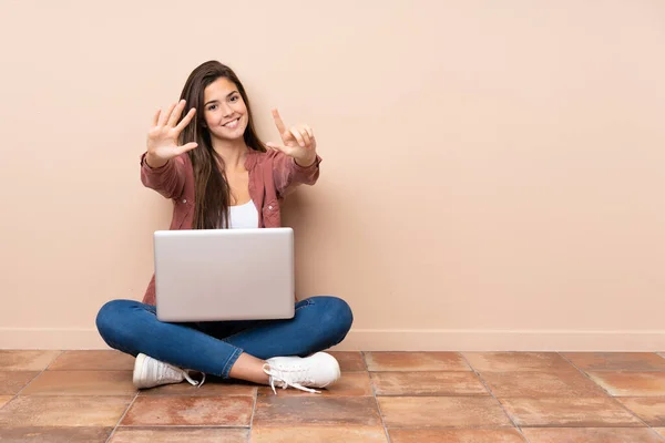 十几岁的女学生坐在地板上 手里拿着笔记本电脑 手里拿着七只手指 — 图库照片