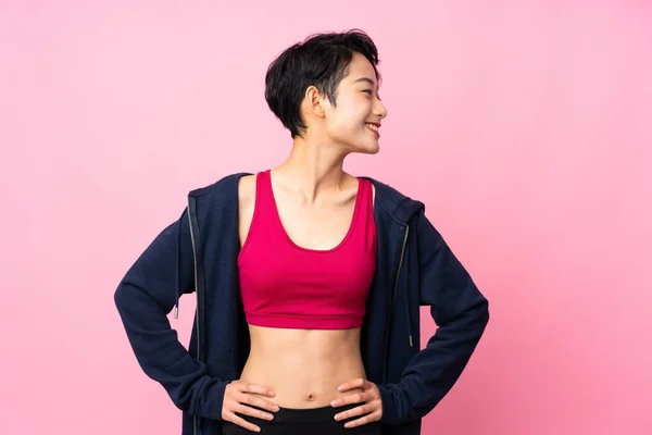 Young sport Asian woman over isolated pink background posing with arms at hip and looking side