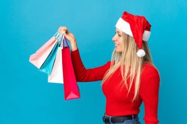 Noel şapkalı bir kadın mavi arka planda izole edilmiş mutlu bir şey alacak.