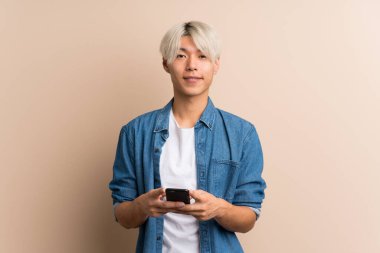 Asyalı genç bir adam izole edilmiş olarak cep telefonuyla mesaj ya da e-posta gönderiyor.