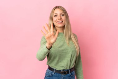 Pembe arka planda izole edilmiş genç sarışın kadın parmaklarıyla beşi sayıyor.