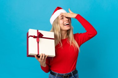 Mavi arka planda izole edilmiş bir hediyeyi tutan Noel şapkalı kadın bir şey fark etti ve çözüme niyetlendi.