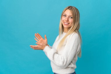 Mavi arka planda izole edilmiş genç sarışın kadın alkışlıyor.