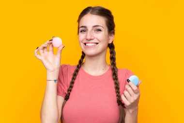 Renkli Fransız badem kurabiyeleriyle izole edilmiş sarı arka planı olan genç bir kadın.