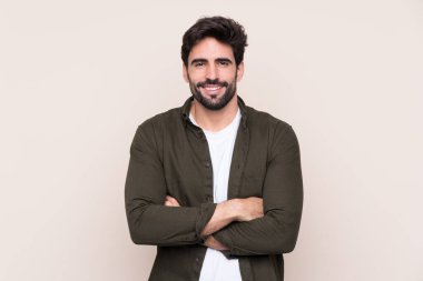 Sakallı, sakallı, genç ve yakışıklı bir adam kollarını ön cephede kavuşturuyor.