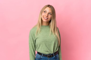 Pembe arka planda izole edilmiş genç sarışın kadın yukarı bakarken bir fikir düşünüyor.