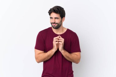 Sakallı, yakışıklı, soyutlanmış beyaz bir arka planı olan genç adam bir şeyler planlıyor.