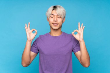 Asyalı genç adam Zen pozunda soyutlanmış mavi arka plan