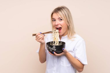 Genç Rus kadın izole edilmiş arka planda elinde çubuklarla bir kase erişte tutuyor ve onu yiyor.