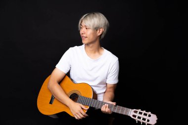 Siyah arka planda gitar çalan Asyalı genç bir adam.