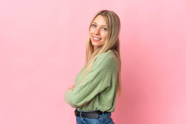 Pembe arka planda soyutlanmış, kolları bağlı ve mutlu genç sarışın bir kadın.