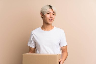 Asyalı genç bir adam izole edilmiş bir arkaplanı başka bir yere taşımak için bir kutu tutuyor.