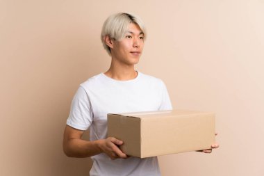 Asyalı genç bir adam izole edilmiş bir arkaplanı başka bir yere taşımak için bir kutu tutuyor.