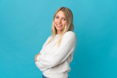 Sarışın genç bir kadın mavi arka planda izole edilmiş, kolları bağlı ve ileriye bakıyor.