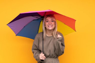 Sarışın bir kadın, sarı bir duvarın üzerinde şemsiye tutuyor ve zaferi kutluyor.