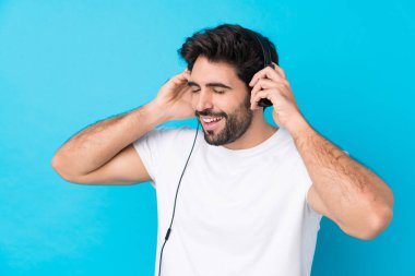 Mavi arka planda sakallı yakışıklı genç adam müzik dinliyor ve şarkı söylüyor.