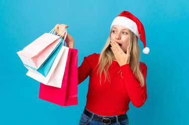 Noel şapkalı kadın mavi arka planda, şaşırmış ve şok olmuş bir yüz ifadesi olan izole edilmiş bir şey alacak.