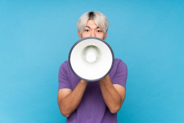 Soyutlanmış mavi arka planda genç Asyalı bir adam megafondan bağırıyor.