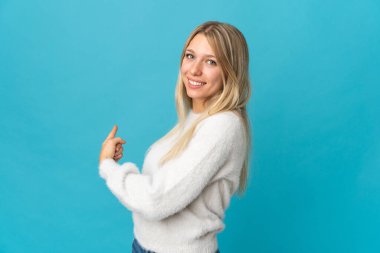 Mavi arka planda izole edilmiş genç sarışın kadın geriye işaret ediyor