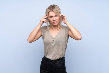 İzole edilmiş mavi arka planı olan genç sarışın kadın mutsuz ve hayal kırıklığına uğramış. Olumsuz yüz ifadesi