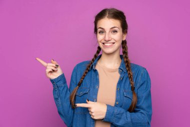 İzole edilmiş mor arka planı olan genç bir kadın parmak uçlarını işaret ediyor.