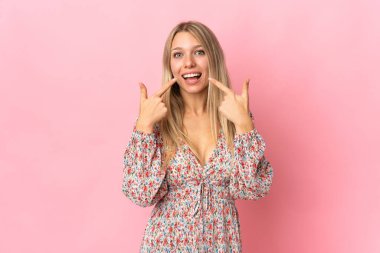 Pembe arka planda izole edilmiş genç sarışın kadın baş parmak işareti yapıyor.