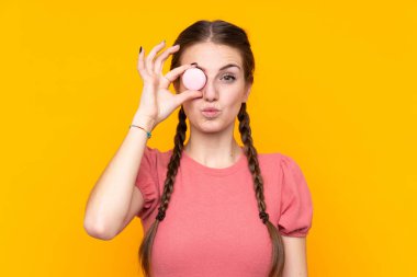 Soyutlanmış sarı arka planda genç bir kadın elinde komik yüzlü renkli Fransız kurabiyeleri var.