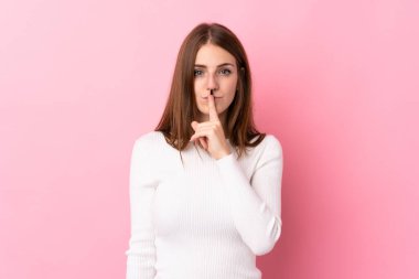 Soyutlanmış pembe arka planda genç bir kadın sessizlik işareti gösteriyor. Parmağını ağzına sok.