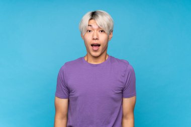 Asyalı genç adam mavi arka planda, şaşırmış bir yüz ifadesi var.