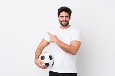 Sakallı yakışıklı bir genç, izole edilmiş beyaz bir arka planı var. Futbol topu ve yan tarafı işaret ediyor.