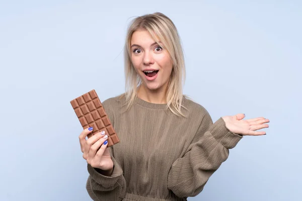 Mladá Blondýna Žena Přes Izolované Modré Pozadí Čokoládovou Tabletu Překvapený — Stock fotografie