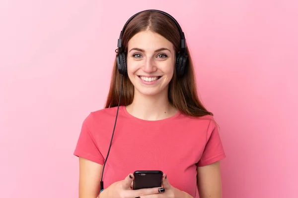 Mujer Joven Sobre Fondo Rosa Aislado Escuchando Música Con Móvil —  Fotos de Stock