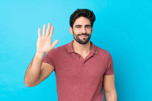 Jovem Homem Bonito Com Barba Sobre Fundo Azul Isolado Saudando — Fotografia de Stock