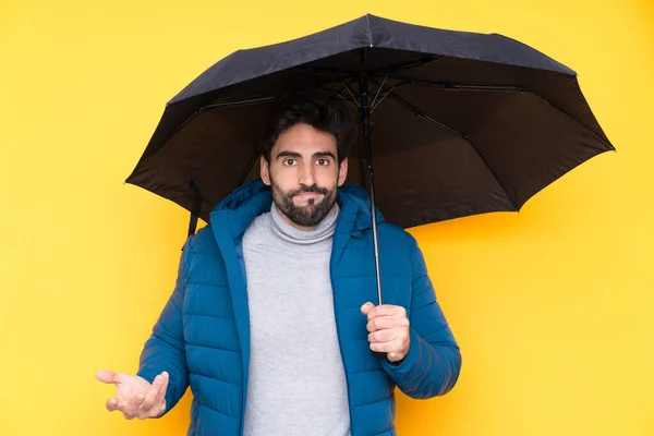肩を持ち上げながら黄色の背景に傘を持っている男は疑問ジェスチャーを作り — ストック写真