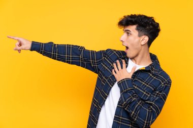 Arjantinli genç adam izole edilmiş sarı arka planda parmağını yana doğru gösteriyor.