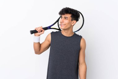 Arjantinli genç adam soyutlanmış beyaz arka planda tenis oynuyor ve yukarı bakıyor.