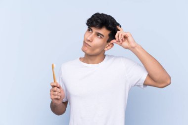 Genç Arjantinli adam dişlerini soyutlanmış mavi arka planda fırçalıyor. Şüpheleri var ve kafası karışmış bir yüz ifadesi var.