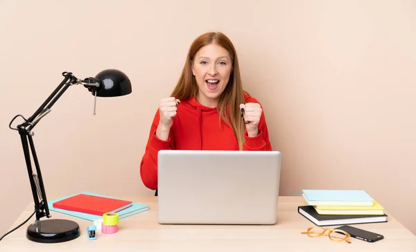 Young student woman in a workplace with a laptop celebrating a victory in winner position
