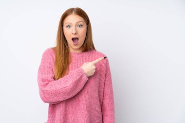 Soyutlanmış beyaz arka planda pembe kazaklı genç, kızıl saçlı kadın şaşırmış ve işaret ediyor.