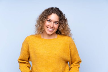 Mavi arka planda saklanmış kıvırcık saçlı genç sarışın kadın gülüyor.