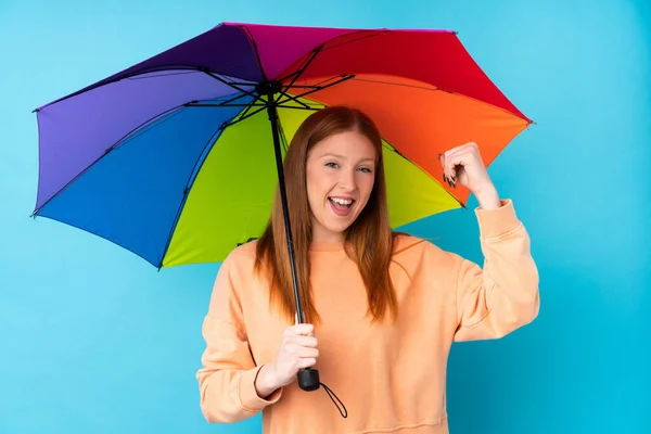 勝利を祝う隔離された壁に傘を持っている若い赤毛の女性 — ストック写真