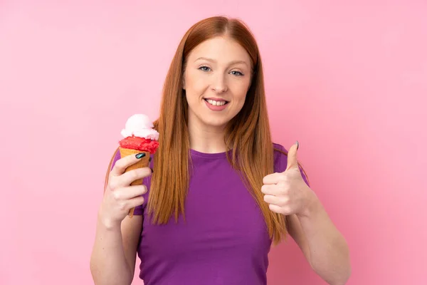若いですRedhead女性とともにCornetアイスクリーム上の隔離されたピンクの背景とともに親指アップ何か良いことが起こっているので — ストック写真