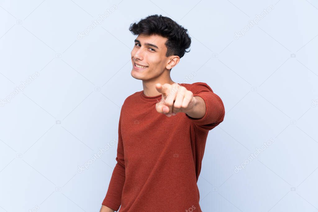 Young Argentinian man over isolated blue background points finger at you with a confident expression